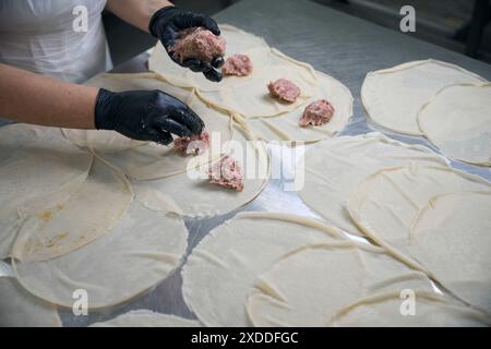 Il lavoratore mette il ripieno di carne sui pancake Foto Stock