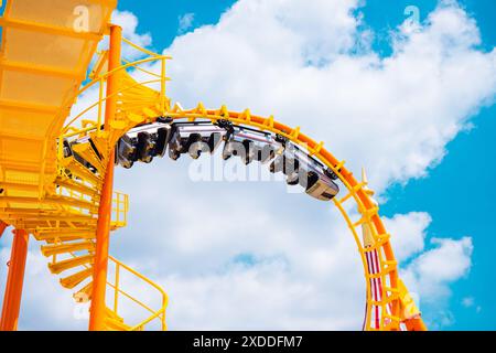 Le montagne russe gialle rotolano la curva del cielo dall'alto al blu attività della stagione estiva divertente al parco divertimenti. Foto Stock