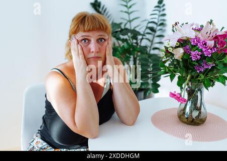 ritrarre una donna di mezza età, in stato d'animo sconvolto, piangere, seduta accanto al tavolo su cui si trovano i fiori del bouquet Foto Stock