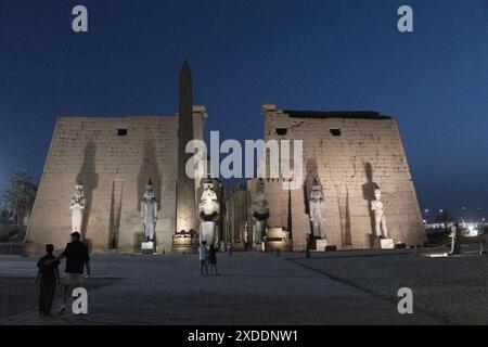 Le sei statue colossali e l'obelisco all'ingresso principale del tempio di Luxor, in Egitto, si illuminano per i visitatori notturni. Foto Stock