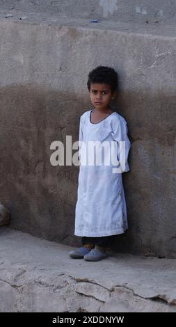 Un bambino egiziano dall'aspetto serio che indossa una tradizionale gallibaya in un villaggio lungo il Nilo vicino a Esna, in Egitto. Foto Stock