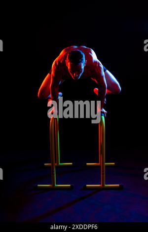 Un atleta maschile forte mostra mosse su barre parallele, riprese in studio Foto Stock
