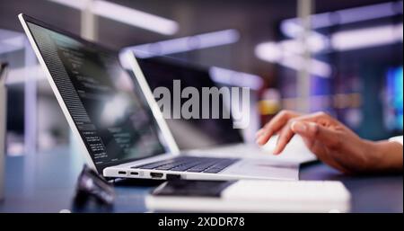 Sito Web di codifica donna afroamericana multi-tasking sul laptop alla scrivania dell'ufficio mentre si ascolta la musica dallo schermo Foto Stock