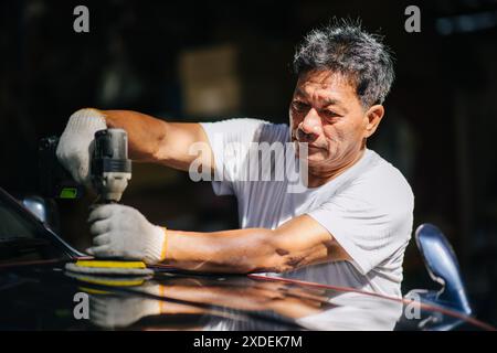 Lucidatrice per auto, lavoratore in officina che utilizza la cera di rivestimento per lucidatrice a colori nella cura delle auto. Foto Stock