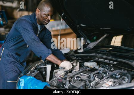 Garage Mechanic African Black maschio lavoro auto auto di lavoro professionale che controlla l'olio motore sul cofano anteriore. Foto Stock