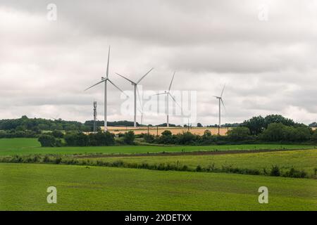 Fila di turbine eoliche in un campo durante l'estate in una giornata nuvolosa Foto Stock