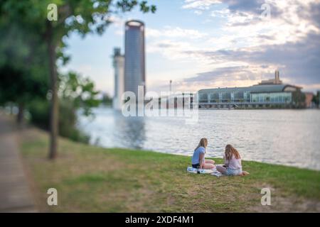 Due persone si godono un pomeriggio tranquillo sul lungofiume di Siviglia, Spagna, con una vista panoramica degli edifici della città. Foto Stock