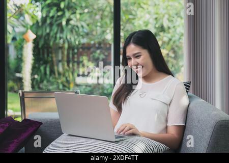 Piuttosto sorridente giovane donna seduta sul divano e di lavoro sul computer portatile Foto Stock