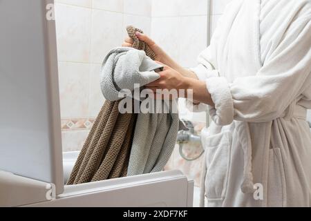 Una ragazza con l'abito bianco prende un asciugamano dalla lavatrice del bagno, lavando le cose, facendo i compiti Foto Stock