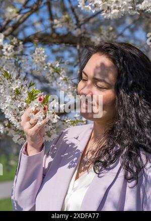 immagine romantica di una donna elegante in una giacca leggera. Positivo, atmosfera primaverile. Una ragazza carina tiene delicatamente un ramo sakura bianco e guarda i fiori Foto Stock