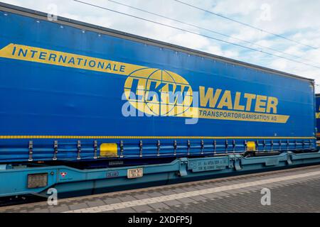 Un container blu, marchiato con il logo „LKW Walter“, è parcheggiato su un carro su binari ferroviari. Ci sono linee elettriche aeree. Foto Stock