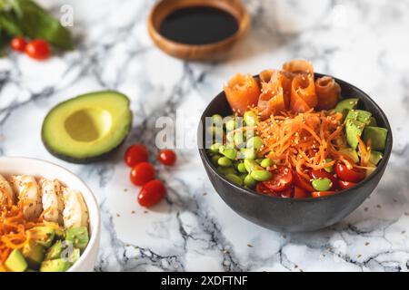 Ciotola nutriente con avocado, edamame, pomodori ciliegini, carote grattugiate, gamberetti e salmone su fondo di marmo. Concetto di cibo sano Foto Stock