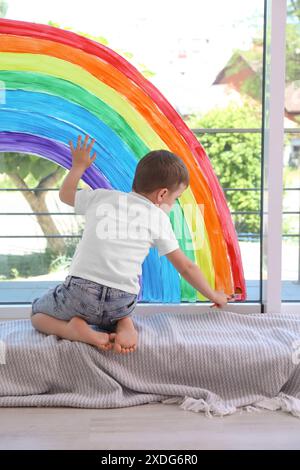 Bambino che disegna l'arcobaleno su una finestra all'interno Foto Stock