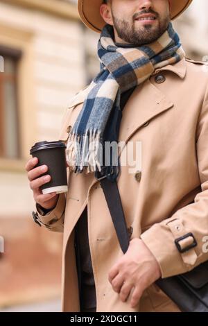 Uomo sorridente in sciarpa calda con tazza di carta all'aperto, primo piano Foto Stock