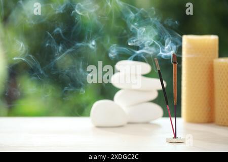 Bastoncini di incenso che si avvicinano a pietre e candele su un tavolo di legno all'aperto, spazio per il testo Foto Stock