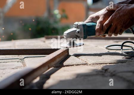 Una persona che utilizza una smerigliatrice angolare per tagliare una barra metallica all'aperto. Le scintille fuoriescono dal processo di molatura. Foto Stock