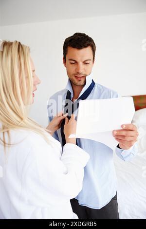 Donna, uomo e aiuto con cravatta al mattino come routine per il lavoro e legare insieme come coppia con cura. Moglie, marito e matrimonio con amore, lavoro di squadra Foto Stock