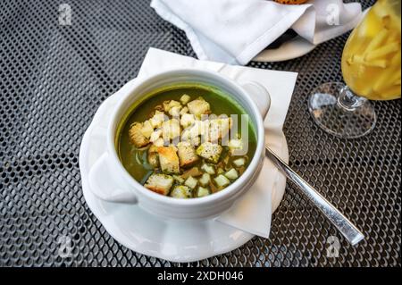 Ciotola con zuppa di spinaci con cubetti di pane fritto e formaggio, zenzero in bicchiere, pasticcini. Cena al ristorante. Foto Stock