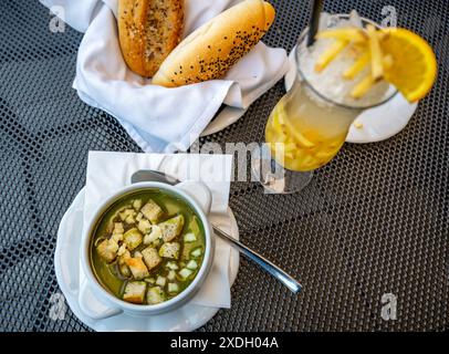 Ciotola con zuppa di spinaci con pane fritto e formaggio, bevanda allo zenzero in bicchiere, pasticcini. Ristorante. Foto Stock