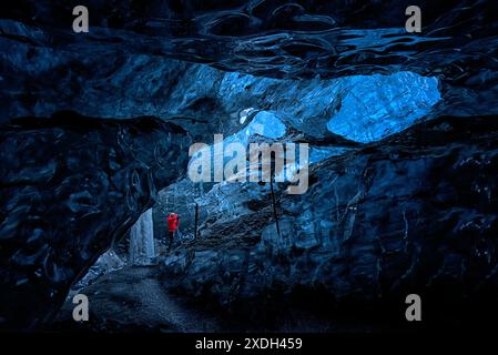 Persona in giacca rossa all'interno di una grotta di ghiaccio glaciale, Islanda. Foto Stock
