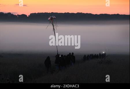 21 giugno 2024, Salisbury, Inghilterra, Regno Unito: Una colonna di fedeli cammina attraverso la nebbia mattutina verso il sole mentre emette un bagliore arancione mentre inizia a sorgere come parte delle celebrazioni del solstizio d'estate a Stonehenge. Stonehenge fu costruita dai primi britannici circa 4000 anni fa per allinearsi al sole sui solstizi. Il solstizio d'estate segna la fine della primavera e l'inizio dell'estate ed è il giorno più lungo e la notte più breve dell'emisfero settentrionale. L'evento è celebrato da migliaia di pagani in tutto il mondo con canti e balli. (Immagine di credito: © Martin Pope/ZUMA Press Wire) EDIT Foto Stock