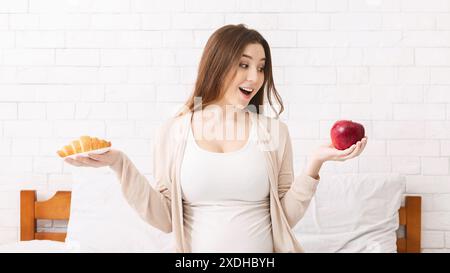 Donna incinta scegliendo tra un croissant e Apple Foto Stock