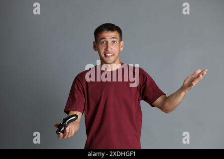 Uomo sorpreso con controller su sfondo grigio Foto Stock