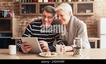 La coppia di anziani che condivide la risata mentre usa il tablet in cucina Foto Stock