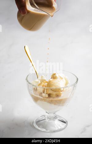 Un primo piano verticale di affogato preparato con espresso versato su gelato alla vaniglia in una tazza di vetro su sfondo bianco Foto Stock