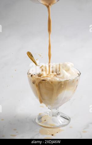 Un primo piano verticale di affogato preparato con espresso versato su gelato alla vaniglia in una tazza di vetro su sfondo bianco Foto Stock