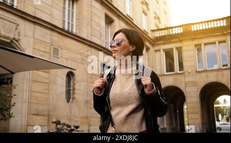 Elegante donna con occhiali da sole passeggia per City Street con zaino Foto Stock