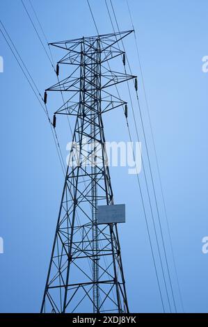 Sagoma di una torre elettrica ad alta tensione contro un cielo blu Foto Stock