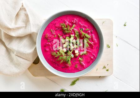 Deliziosa zuppa di barbabietole estive fredda con cetriolo e aneto nel recipiente su fondo bianco in legno. Disintossicazione sana o concetto di cibo vegetariano. Vista dall'alto, f Foto Stock