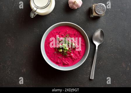 Zuppa di crema di barbabietole con yogurt, cetrioli e aneto nel recipiente su sfondo scuro. Zuppa fredda estiva. Vista dall'alto, disposizione piatta Foto Stock