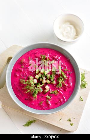 Zuppa di barbabietole estive fredda fatta in casa con cetriolo e aneto nella ciotola su sfondo bianco in legno. Disintossicazione sana o concetto di cibo vegetariano. Vista dall'alto, fl Foto Stock