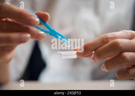 Lady mette una lente a contatto in un contenitore con del liquido Foto Stock