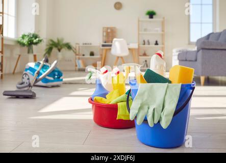 Secchio e lavabo pieni di bottiglie di detergente, guanti in gomma e altri strumenti per la pulizia sul pavimento di casa Foto Stock