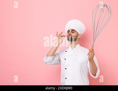 Buon pasticcere con grande frusta su sfondo rosa Foto Stock