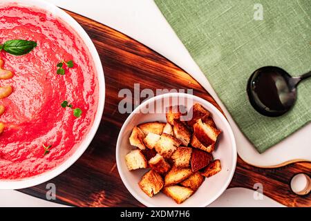 Deliziosa zuppa di crema di pomodoro con sedano e basilico in una ciotola bianca su un asse di legno con crostini su sfondo chiaro. Foto di alta qualità Foto Stock