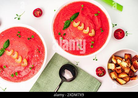 Zuppa di verdure italiane fredda Gazpacho con pomodoro con sedano, basilico e microverdure su un tavolo bianco con crostini. Foto di alta qualità Foto Stock