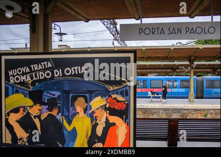 23 giugno 2024, Roma, Italia: il cartone raffigurante l'inaugurazione della ferrovia Roma-Lido nel 1924 con lo slogan "nuovo percorso Roma Lido di Ostia" e, sullo sfondo, un treno moderno si fermò e una persona in attesa dell'arrivo del prossimo treno per Ostia alla stazione di porta San Paolo a Roma. Inaugurata nel 1924, la ferrovia urbana Roma-Lido è lunga 28,359 km e collega la stazione di porta San Paolo, nel quartiere Ostiense, alla stazione Cristoforo Colombo, nel quartiere Lido di Castel Fusano a Ostia, 10° comune di Roma, attraversando 13 stazioni di superficie. Nel 2022, la direzione Foto Stock