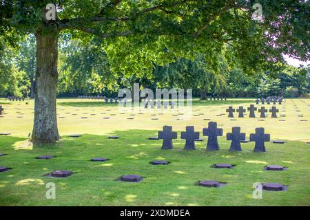 Vista tranquilla del cimitero militare tedesco in Normandia, Francia, con croci di pietra sotto alberi lussureggianti in una giornata di sole. Foto Stock