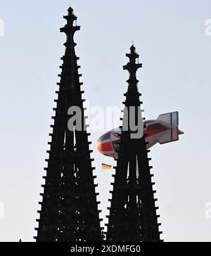 Colonia, Germania. 23 giugno 2024. Calcio, UEFA Euro24, Svizzera - Germania, turno preliminare, gruppo A, giorno 3: un dirigibile con bandiera tedesca può essere visto dietro le guglie della Cattedrale di Colonia. Crediti: Roberto Pfeil/dpa/Alamy Live News Foto Stock