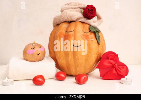 Zucche con volti disegnati, scatola regalo a forma di cuore, cuori e macchie sotto gli occhi su sfondo chiaro Foto Stock