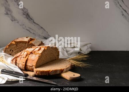 Tavola di legno con pane a fette, spikelets di grano e coltello sul tavolo nero Foto Stock