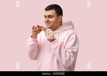 Giovane con un pezzo di gustosa pizza su sfondo rosa Foto Stock