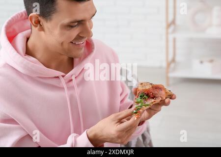 Giovane con un pezzo di gustosa pizza a casa Foto Stock