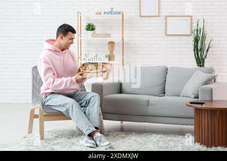 Giovane uomo che tiene in mano una scatola di cartone con gustosa pizza a casa Foto Stock