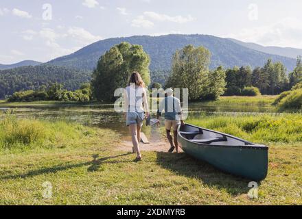 Coppia amorevole che si gode la giornata estiva sul lago, tirando una canoa in acqua, pronta per un'avventura in giro. Foto Stock
