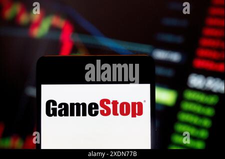 In questa immagine, il logo di GameStop Corp (NYSE: GME), il rivenditore americano di prodotti per videogiochi, elettronica di consumo e prodotti di gioco, è stato visualizzato su uno smartphone con un grafico dell'indice di borsa economica sullo sfondo. Foto Stock